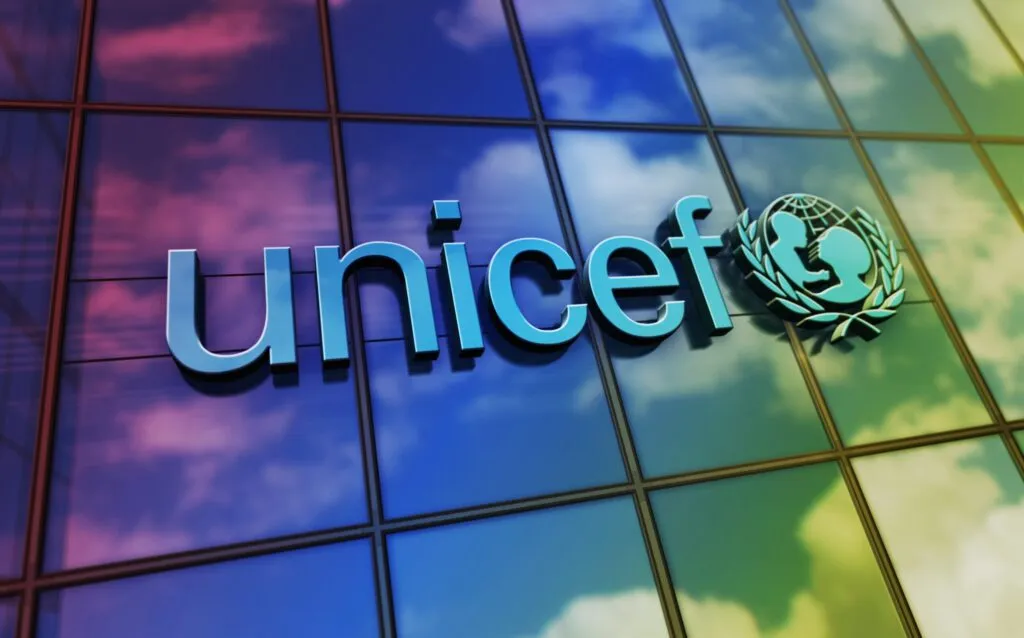 Logotipo de UNICEF en la fachada de un edificio de vidrio con reflejo del cielo, imagen para portada de artículo sobre apoyo de UNICEF en salud y nutrición para niños desplazados en Siria.