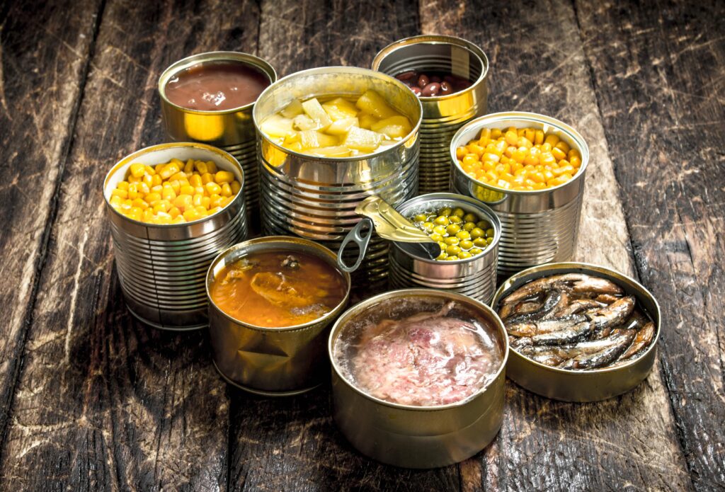 Latas abiertas con verduras, frutas, legumbres, pescado y carne, ejemplo de alimentos envasados y procesados que pueden contener químicos invisibles que afectan la salud.
