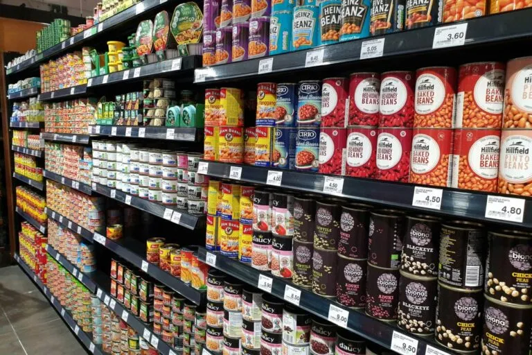 Estantes de supermercado repletos de alimentos ultraprocesados enlatados que muestran cómo estos productos reducen la saciedad y aumentan la ingesta calórica diaria