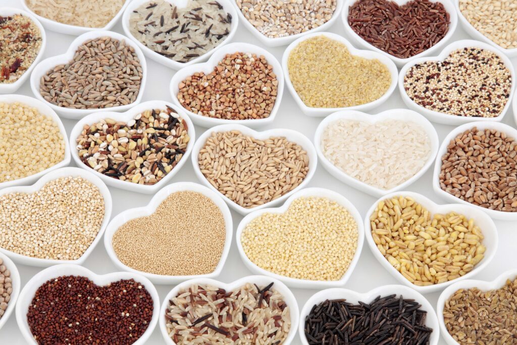 Diferentes tipos de granos saludables como avena, quinua y amaranto presentados en recipientes blancos en forma de corazón, representando nutrición y bienestar