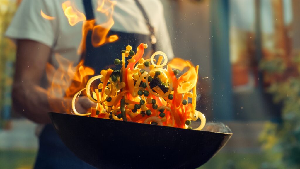 Verduras frescas salteadas en un wok con fuego, representando la cocina casera y saludable de la serie Raid the Kitchen en YouTube.