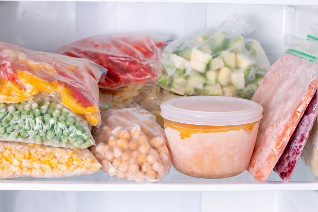 Alimentos congelados en bolsas y recipientes dentro de un congelador, ilustrando prácticas seguras para descongelar alimentos y evitar intoxicación alimentaria.