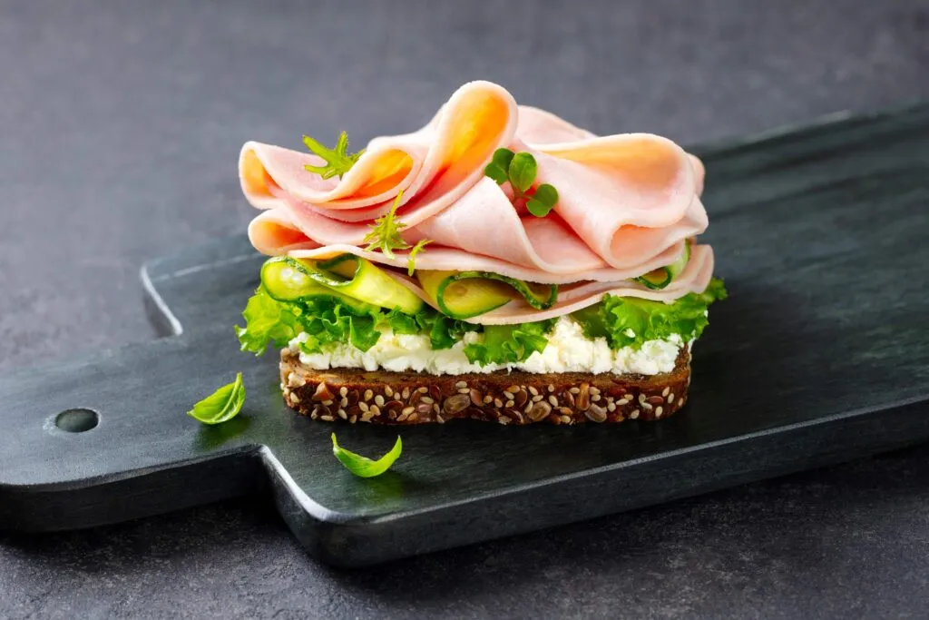Sandwich abierto de pan integral con jamón, queso fresco y vegetales verdes que ilustran las mejores opciones de jamón con más proteínas y menos grasa según Profeco.