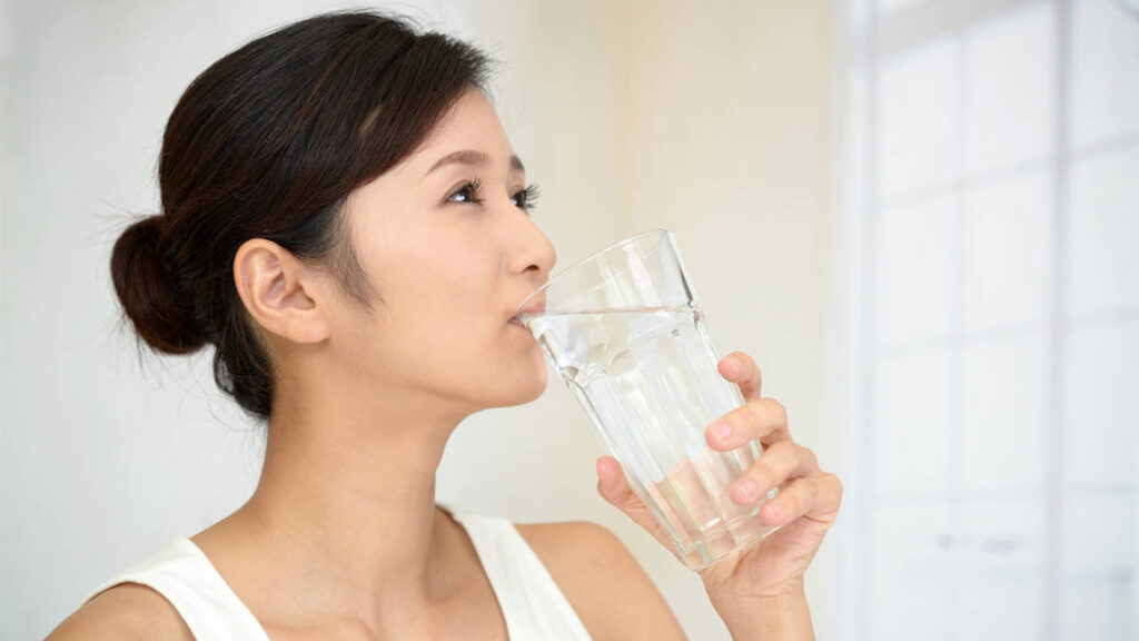 Mujer inicia su día bebiendo agua tibia en ayunas para mejorar digestión y bienestar según el método sayu.