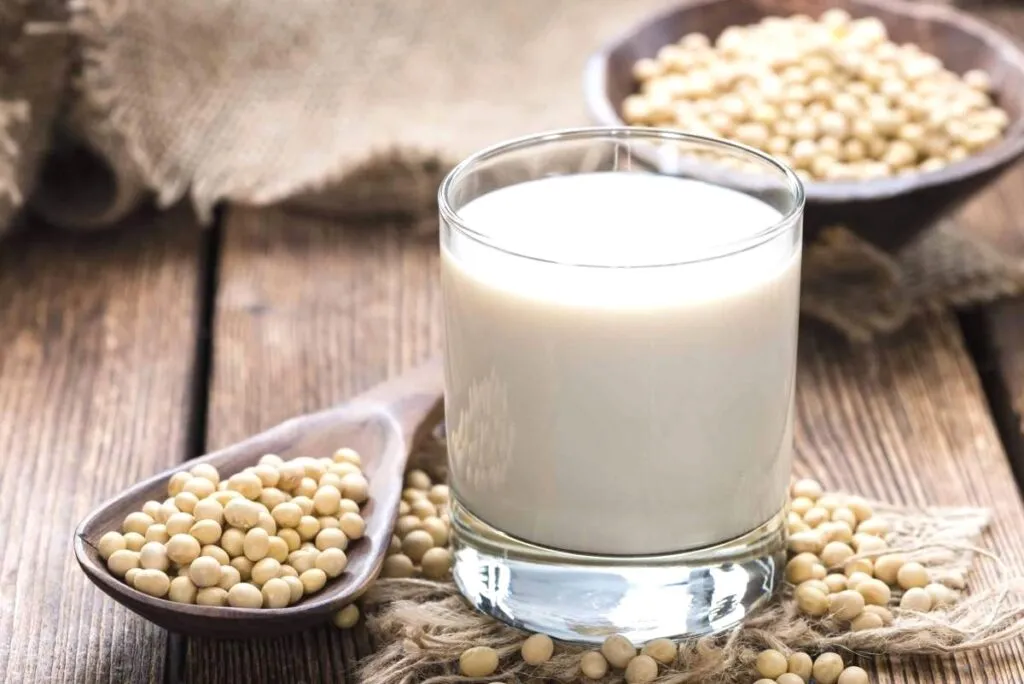 Vaso de leche vegetal con presencia de almendras y frijoles de soja, ilustrando comparación saludable.