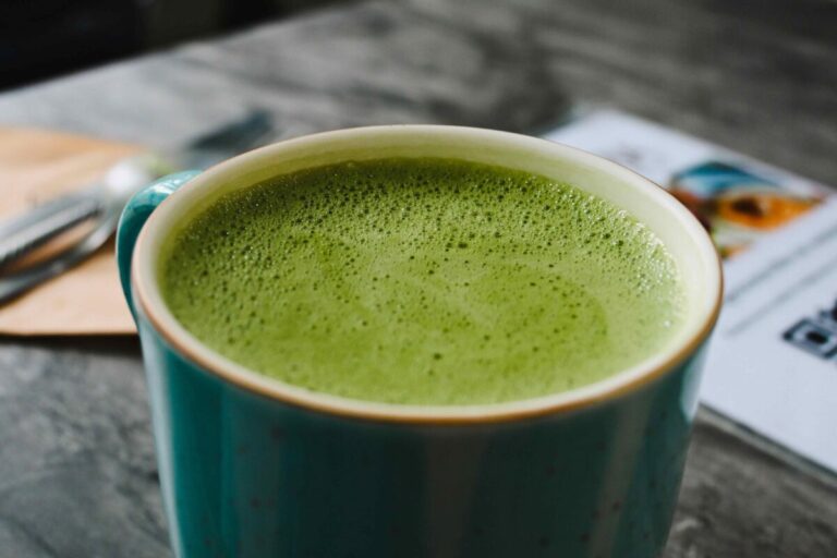 Tazas de té y matcha junto a vegetales ricos en hierro, mostrando su impacto en la absorción de hierro
