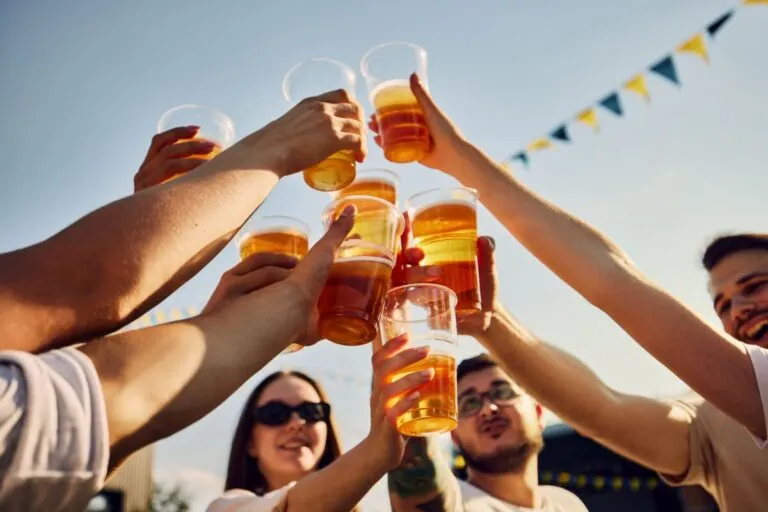 Grupo de personas brindando con vasos de cerveza al aire libre, representando el consumo de cervezas con alto contenido de azúcar según Profeco.