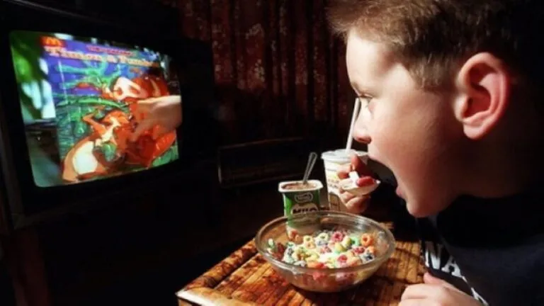Niño frente a la televisión durante una comida, ilustrando el impacto en la nutrición infantil