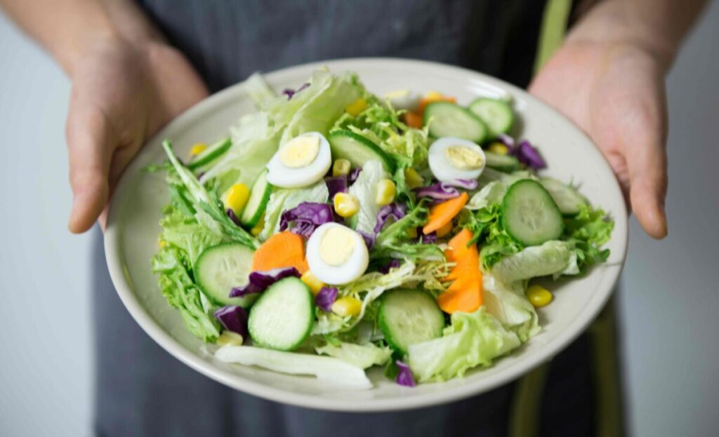 Mujer sosteniendo un bowl con vegetales crudos frente a su abdomen para aliviar el estreñimiento