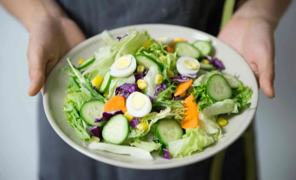 Mujer sosteniendo un bowl con vegetales crudos frente a su abdomen para aliviar el estreñimiento