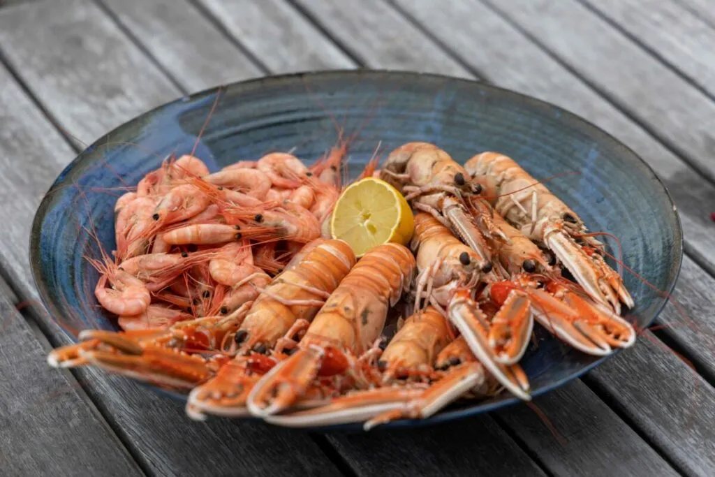 Plato de gambas con persona chupando la cabeza, riesgo de cadmio en mariscos