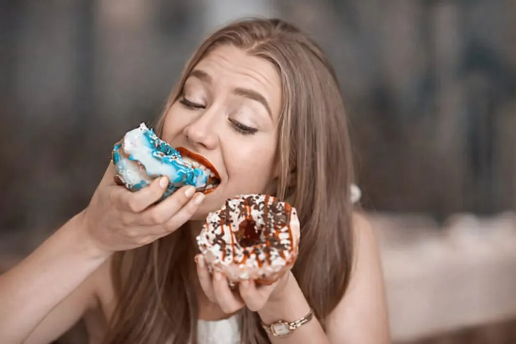 Mujer con antojos intensos comiendo donas azucaradas, ejemplo visual para controlar antojos
