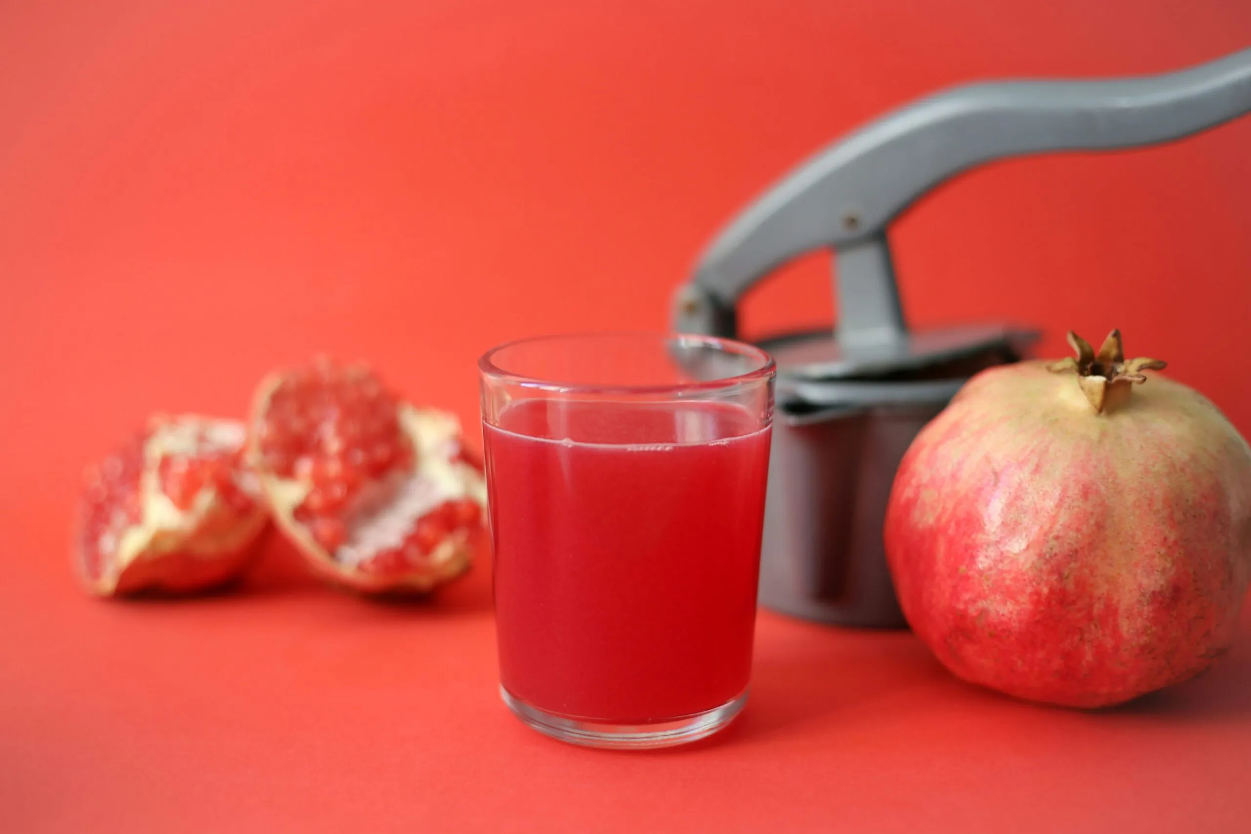 Vaso de jugo de granada y granadas frescas mostrando beneficios para la salud cardiovascular