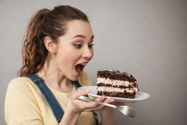 Mujer joven con antojos menstruales observando con deseo una rebanada de pastel de chocolate