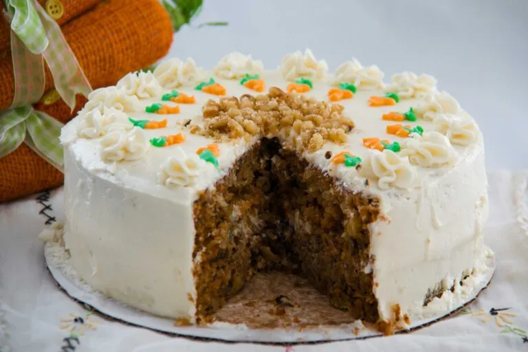 Rebanada de carrot cake húmedo y saludable con cobertura suave, rodeada de ingredientes naturales como zanahorias y nueces
