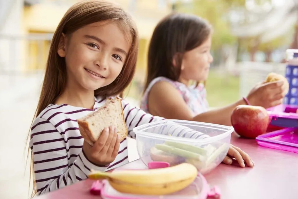 Estudiantes comiendo frutas y alimentos saludables en comedor escolar como parte de políticas de alimentación saludable en escuelas.
