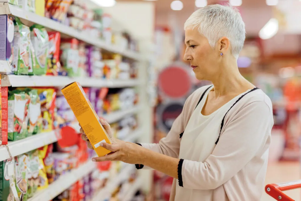 Persona revisando etiquetas nutricionales de productos alimenticios mientras compara opciones en un supermercado.