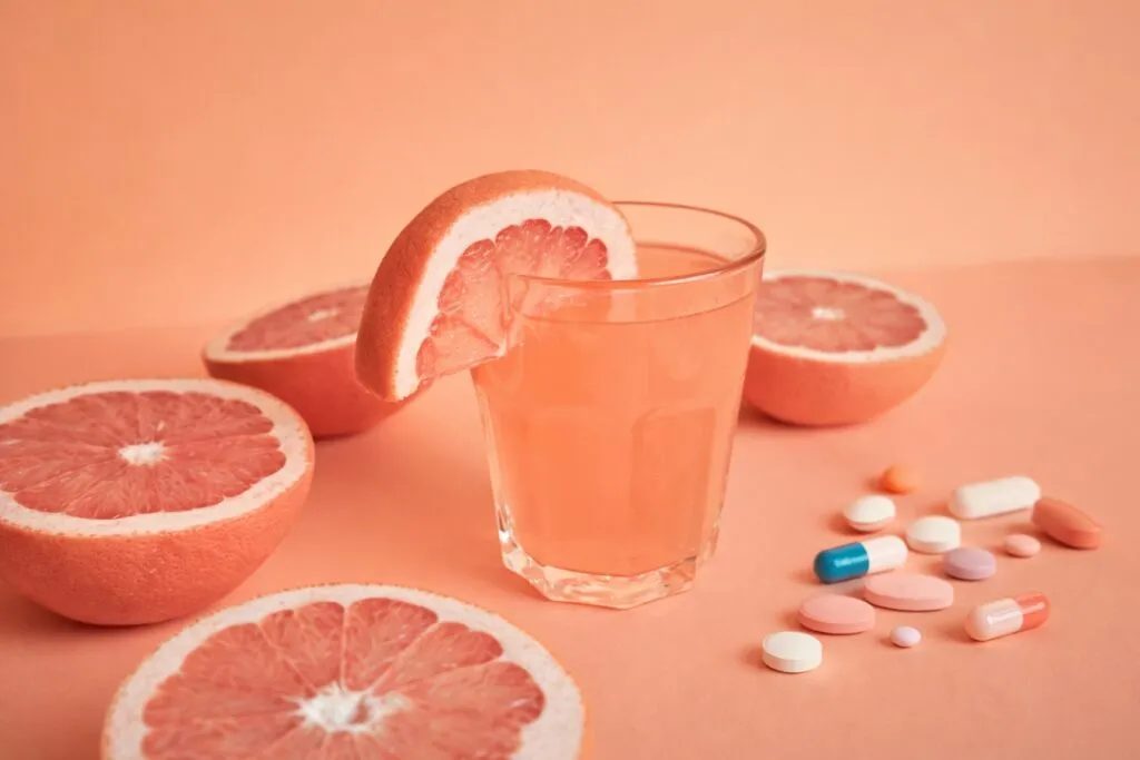 Vaso de jugo de toronja junto a pastillas mostrando riesgo de interacción con medicamentos en el organismo