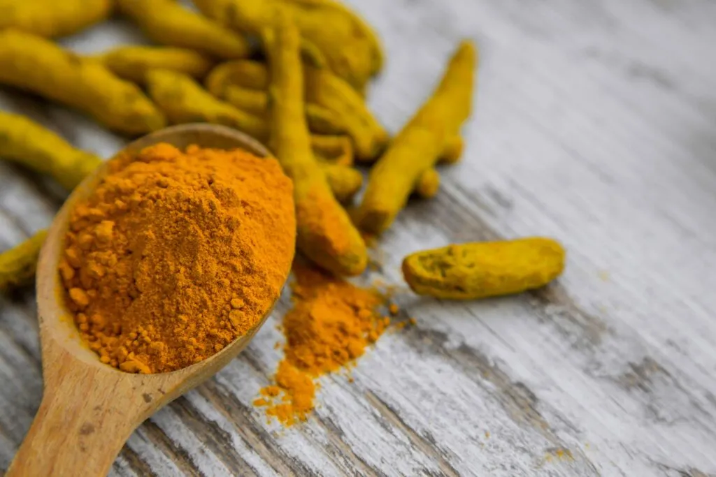 Cúrcuma diaria en polvo junto a una cuchara y alimentos saludables para una nutrición equilibrada