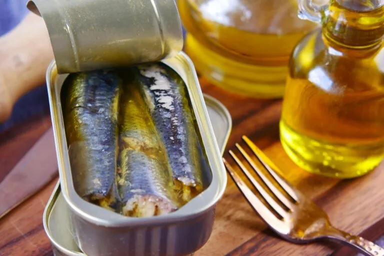 Lata abierta de sardinas acompañada de pan integral, limón y ensalada, representando una alimentación saludable con sardinas en lata.