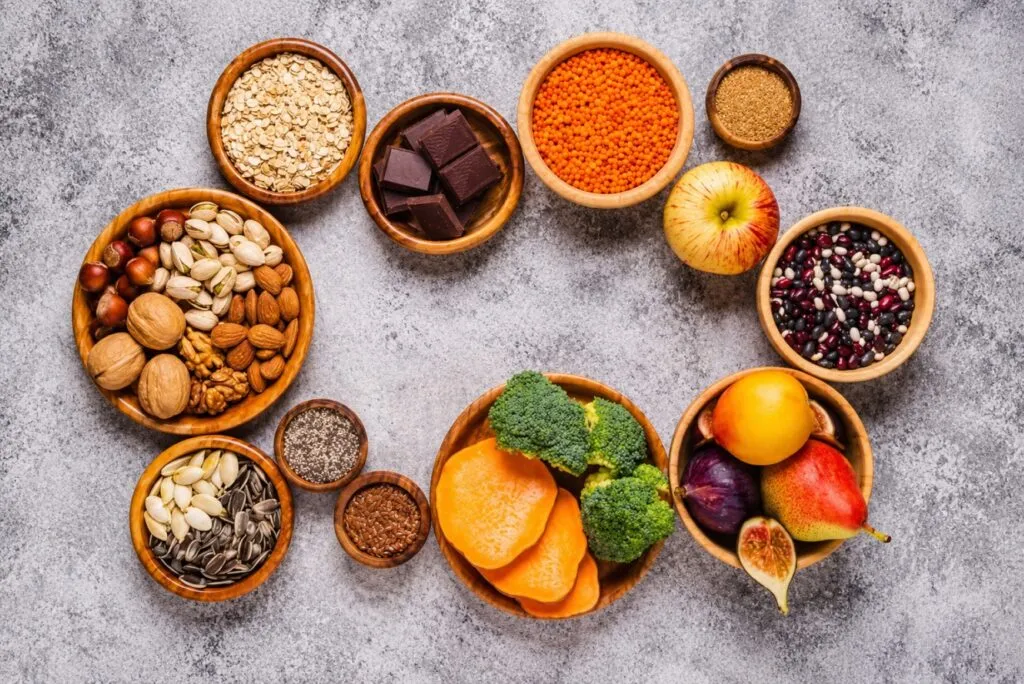 Alimentos con fibra como chía, frijoles, frambuesas y aguacate junto a un tazón de avena