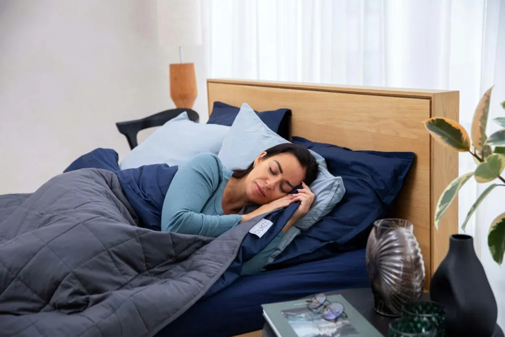 Persona preparándose para dormir mejor en un dormitorio oscuro, tranquilo y ordenado, siguiendo hábitos para un descanso reparador.