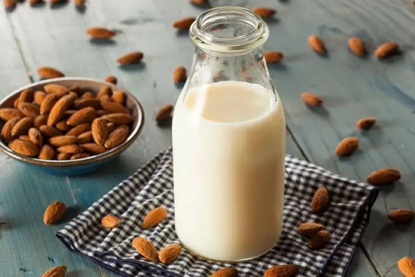 Vaso de bebida vegetal acompañado de avena, almendras y soya como diferentes alternativas vegetales