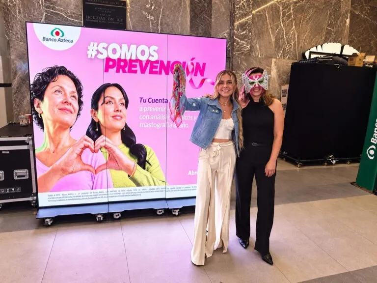 Dos mujeres posan frente a una pantalla de Banco Azteca con la campaña SOMOS Prevención durante un encuentro de Mujeres en Lucha.